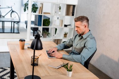 yakışıklı işadamı modern ofiste otururken dizüstü bilgisayarda yazarak