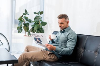 kanepede oturan ve iş Gazete okurken Kupası tutan işadamı