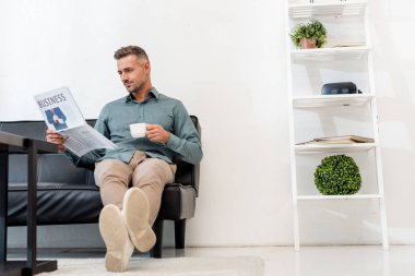 mutlu işadamı iş gazetesi ve içkiyle Kupası okurken kanepede oturan