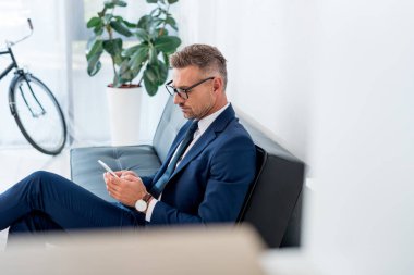 seçici odak kanepede otururken smartphone kullanarak ciddi iş adamı