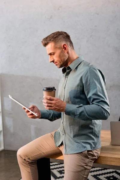 Przystojny Biznesmen Trzymając Kubek Jednorazowy Patrząc Cyfrowych Tablet Biurze — Zdjęcie stockowe