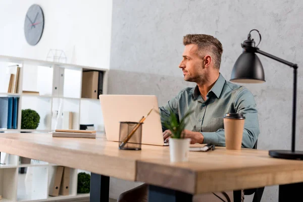 近代的なオフィスにラップトップのそばに座ってハンサムな実業家 — ストック写真