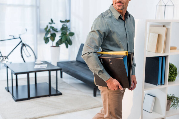 cropped view of cheerful businessman standing with folders in modern office