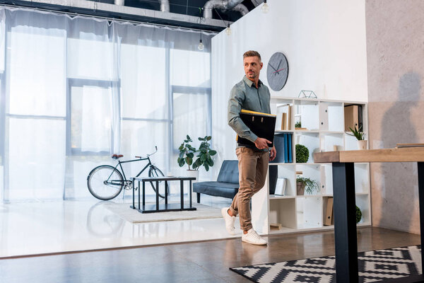 confident businessman standing with folders in modern office