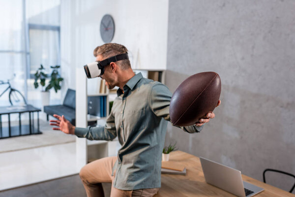 businessman wearing virtual reality headset and holding american football in offcie