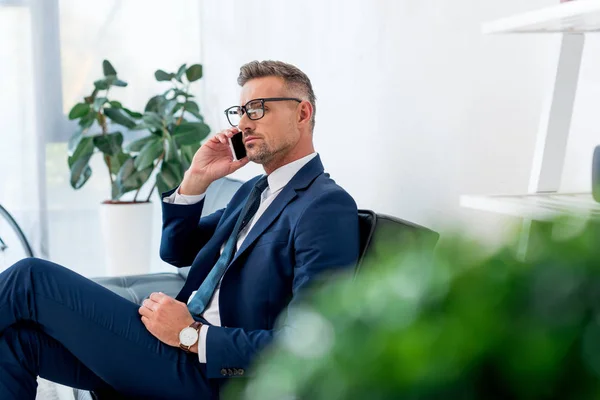 Selective Focus Serious Businessman Talking Smartphone While Sitting Sofa — Stock Photo, Image