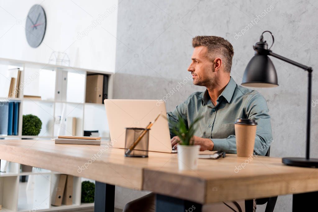 handsome businessman sitting near laptop in modern office