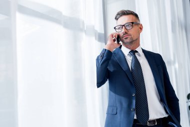 Takım elbiseli yakışıklı iş adamı ayakta duruyor ve akıllı telefonla konuşuyor.