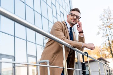 bej bir palto ayakta ve smartphone üzerinde konuşmak mutlu işadamı 