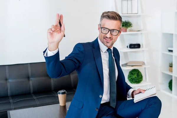 Cheerful Businessman Glasses Smiling While Gesturing Holding Notebook Pen — Stock Photo, Image