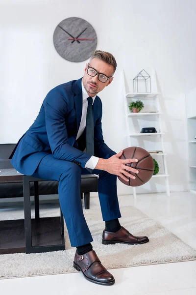 Pohledný Podnikatel Obleku Drží Basketbal Rukou Zatímco Sedí Konferenční Stolek — Stock fotografie