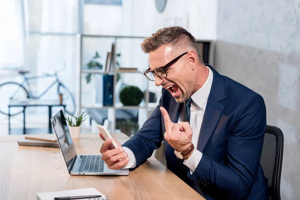 Emotional Businessman Glasses Suit Screaming While Holding Smartphone Showing Middle — Stock Photo, Image