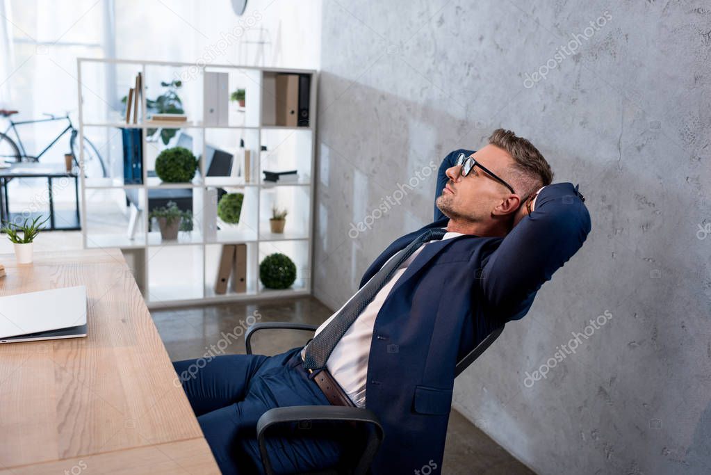 handsome businessman in glasses relaxing near laptop in office