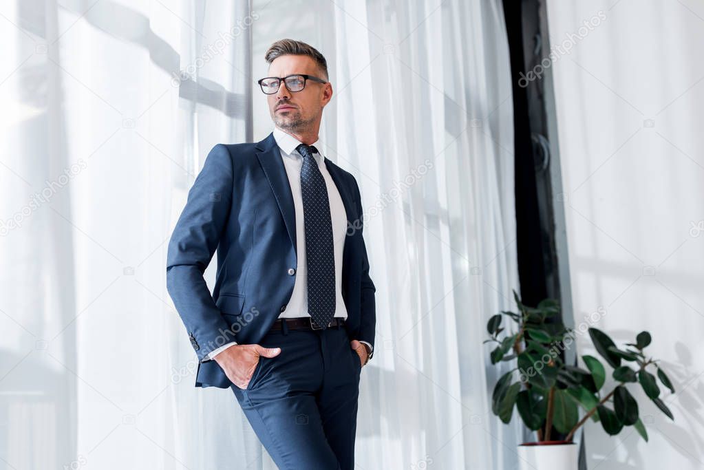 confident businessman in suit and glasses standing with hands in pockets 