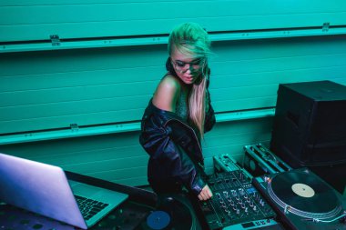 sexy blonde dj girl in glasses touching dj mixer in nightclub  clipart