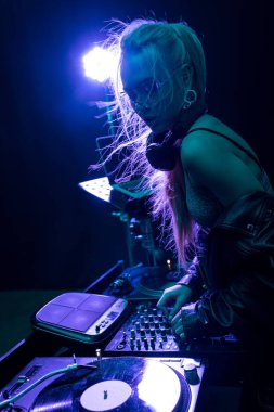 stylish dj girl touching dj equipment while standing in nightclub  clipart