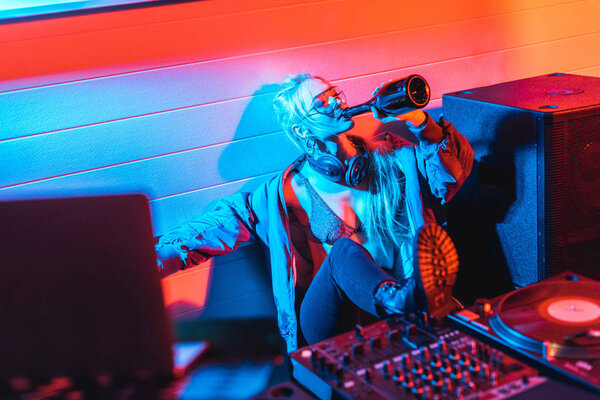 selective focus of attractive dj woman drinking wine from bottle with closed eyes