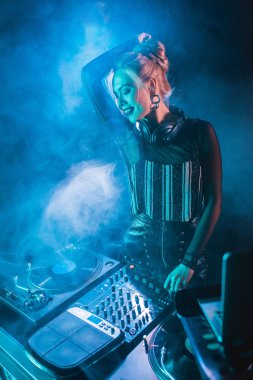 Dumanlı gece kulübünde dj ekipmanları yakın duran Kulaklığımda mutlu sarışın dj kız 