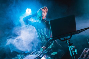 DJ ekipmanları dokunmaktan ve gece kulübünde duman ile gülümseyen şık sarışın dj kız 