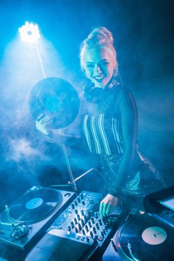 DJ ekipmanları dokunmaktan ve duman ile gece kulübünde retro vinil kaydı tutan gülümseyen sarışın dj kız 