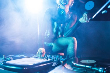 retro vinil tutan neşeli dj kadın görünümünü kırpılmış kayıt ve ayakta yakın dumanlı gece kulübünde dj ekipmanları: 