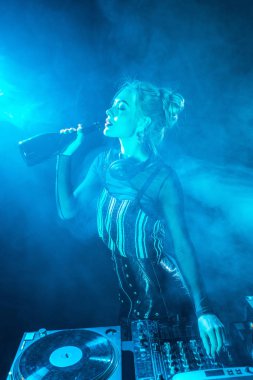 sarışın dj kadın dumanlı gece kulübünde dj ekipmanları yakınındaki şişe şarap içme kulaklık