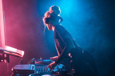 DJ dj mikser kullanarak ve vinil kaydı duman ile gece kulübünde dokunmadan sarışın kadınla
