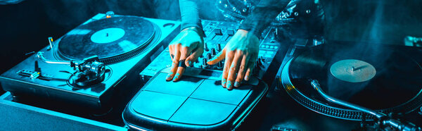 panoramic shot of dj girl using dj equipment in nightclub with smoke 