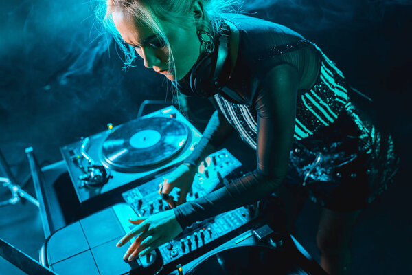 сфокусированный красивый ди-джей девушка с помощью диджея оборудования в ночном клубе с дымом
 