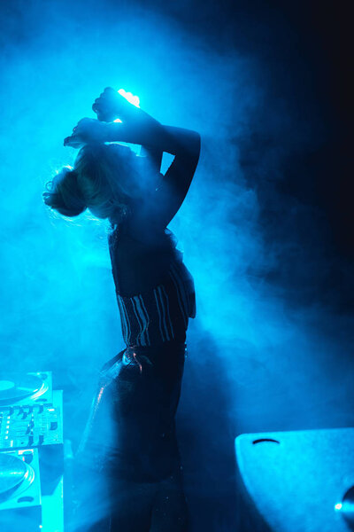 silhouette of dj woman standing in nightclub with smoke  