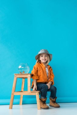 kid in jeans and orange shirt sitting on stairs with glass fishbowl clipart
