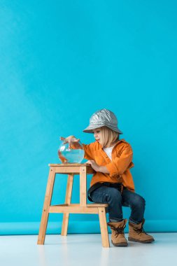 kid in jeans and orange shirt sitting on stairs and playing with goldfish  clipart