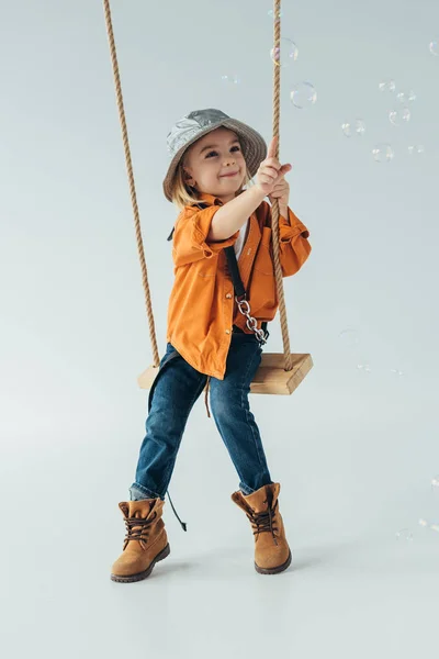 Улыбающийся Ребенок Джинсах Оранжевой Рубашке Сидящий Качелях Взмахивающий Пальцем Мыльные — стоковое фото