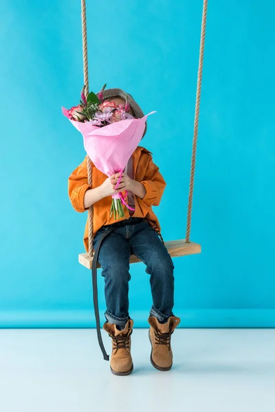 Kind Sitzt Auf Schaukel Und Hält Blumenstrauß Auf Blauem Hintergrund — Stockfoto