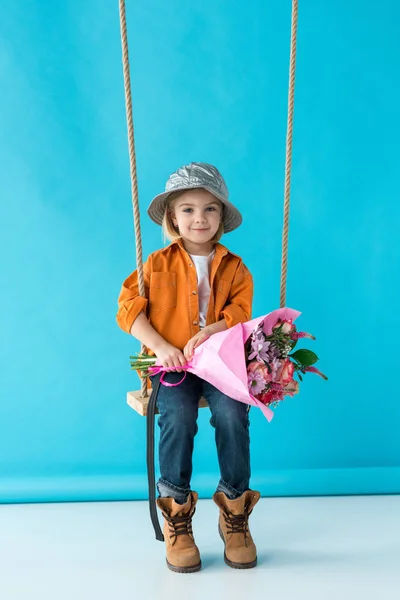 Adorable Kid Sitting Swing Holding Bouquet Looking Camera Blue Background — Stock Photo, Image