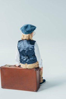 arkadan görünüşü retro yelek çocukta ve bavul gri arka plan üzerinde oturan kap