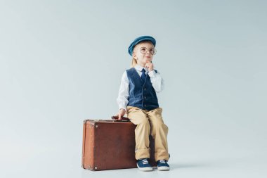 retro yelek ve bavul gri arka plan üzerinde oturan kap dalgın çocuk 
