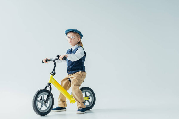 thoughtful kid in retro vest and cap riding bicycle and looking away 