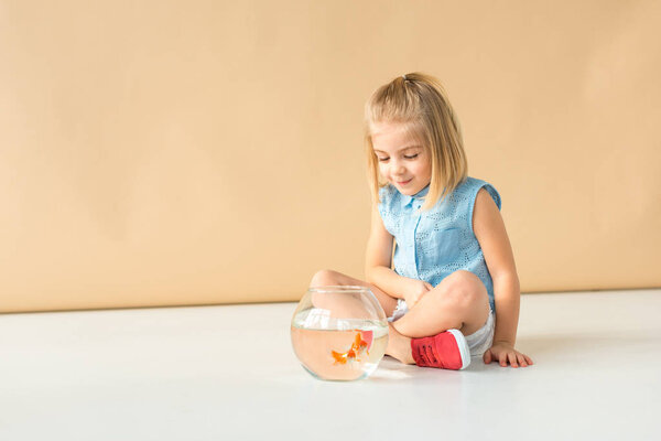 cute kid sitting with crossed legs and looking at fishbowl
