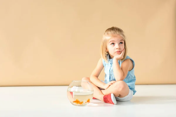 Dreamy Kid Sitting Floor Fishbowl Looking Away Beige Background — Stock Photo, Image