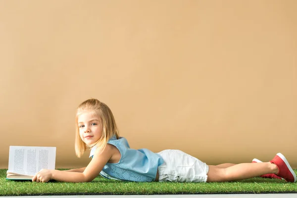 Lindo Niño Acostado Alfombra Hierba Celebración Libro Sobre Fondo Beige — Foto de Stock