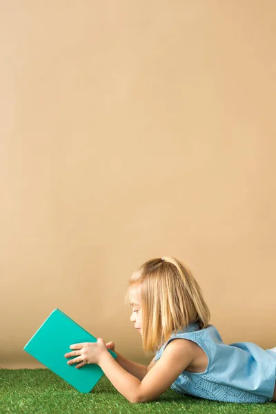 Kid Liggande Gräs Matta Och Läsa Bok Beige Bakgrund — Stockfoto