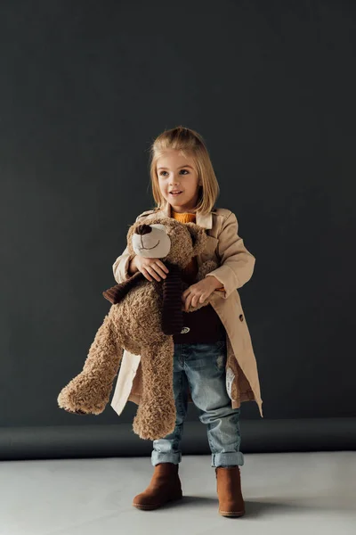 Lachende Schattig Kind Trenchcoat Jeans Holding Teddybeer Zwarte Achtergrond — Stockfoto
