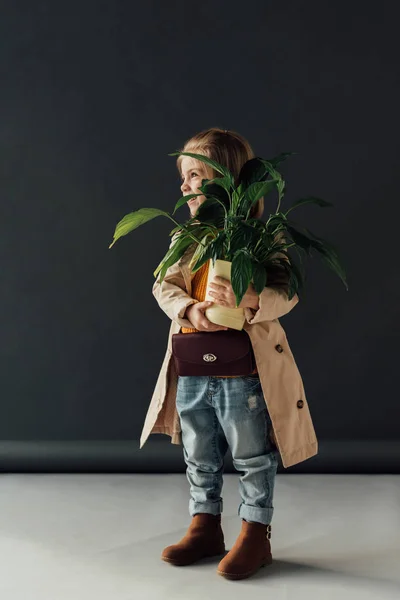 トレンチ コートと黒い背景に植木鉢に植物を保持しているジーンズでかわいい子 — ストック写真