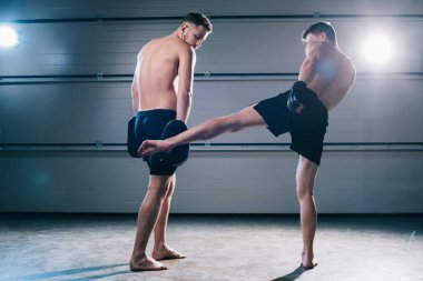 back view of strong muscular barefoot mma fighter practicing low kick with another sportsman  clipart