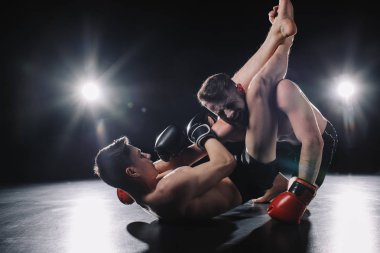 strong mma fighter in boxing gloves doing painful chokehold with legs to another sportsman on floor clipart