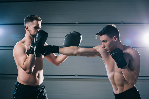 athletic muscular shirtless mma fighter practicing punch with another sportsman during training