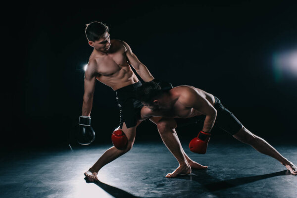 shirtless strong muscular mma fighter in boxing gloves clinching another 