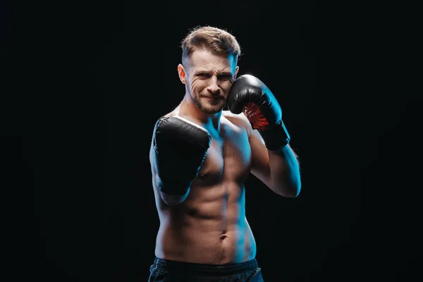 muscular shirtless strenuous boxer in boxing gloves doing punch at camera isolated on black
