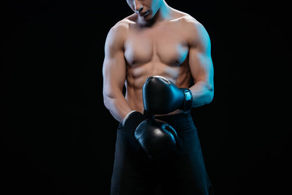 partial view of muscular shirtless boxer in boxing gloves isolated on black